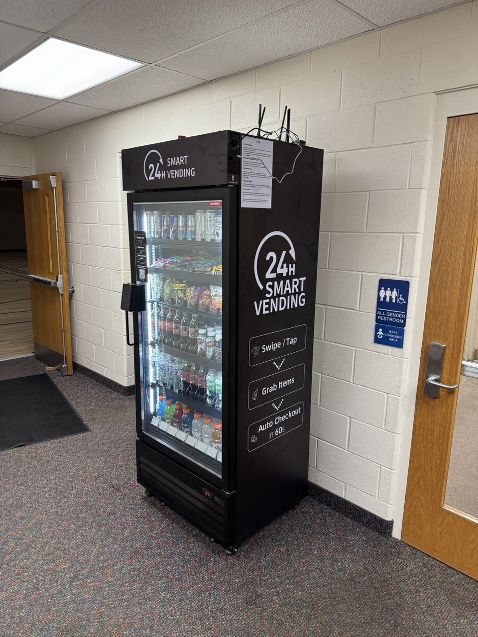 A wrapped Tap N Take Max 620 smart vending cooler stocked with drinks and snacks at the Spencer YMCA in Spencer, Indiana