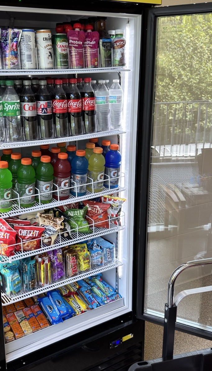 Open Tap N Take smart cooler showing shelves stocked with drinks, snacks, protein bars and candy at the YMCA Northwest Branch in Bloomington, Indiana